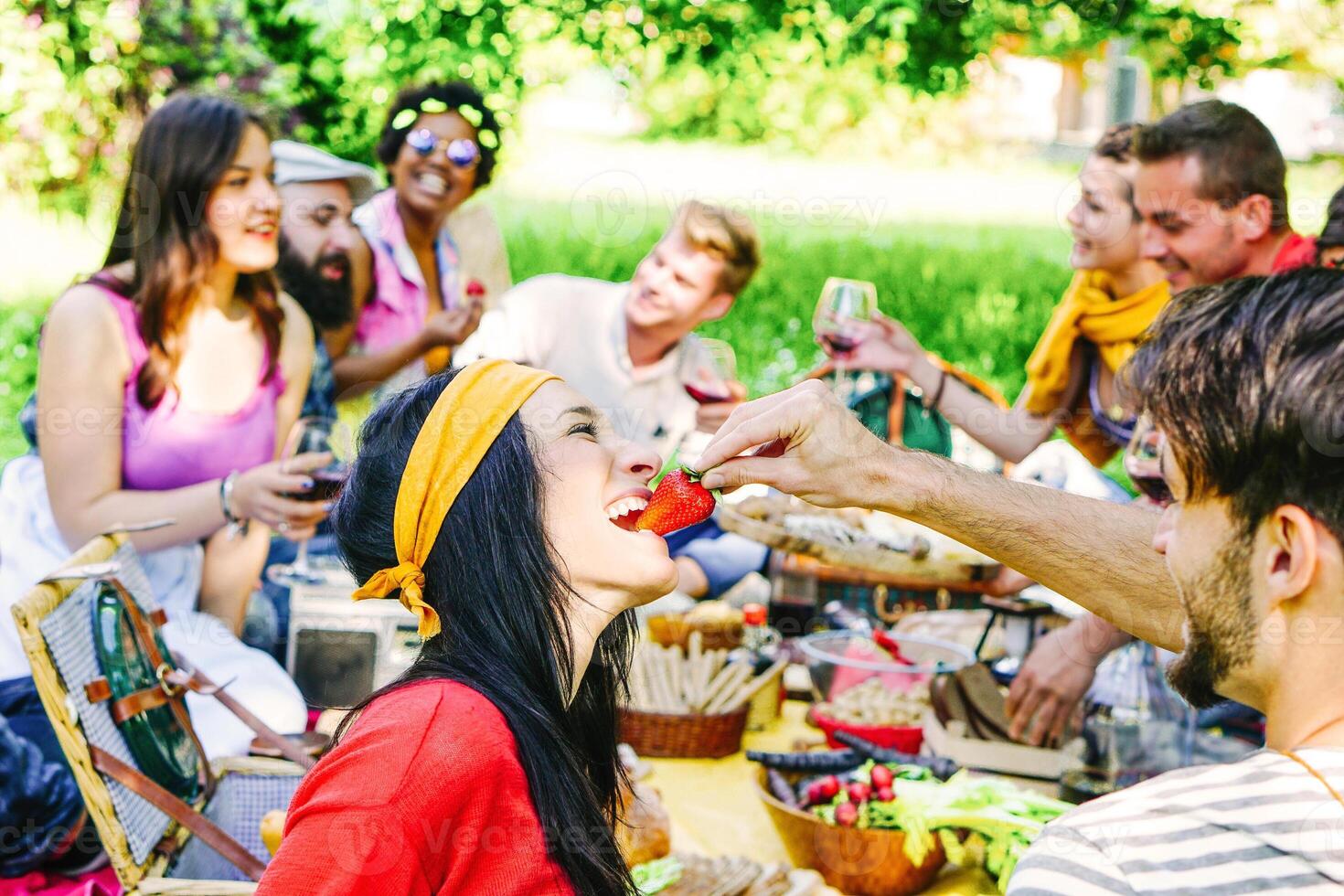 contento amigos haciendo un picnic en el jardín al aire libre - joven de moda personas teniendo divertido comiendo y Bebiendo mientras sentado en el césped en el naturaleza - juventud, amistad, comida concepto - atención en hembra foto