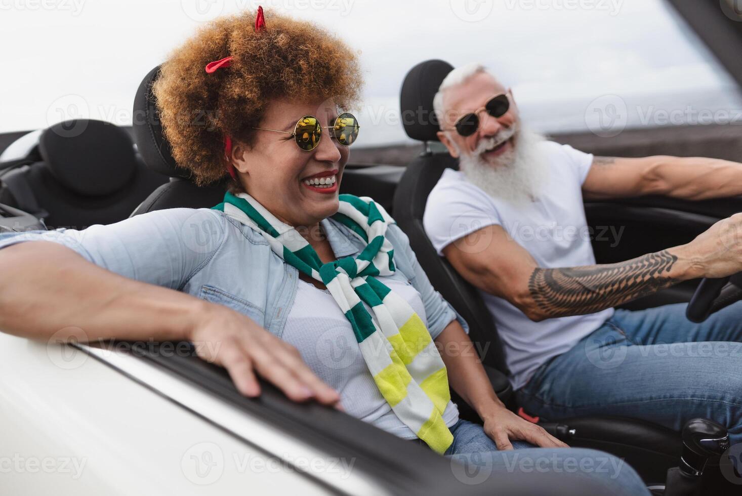 Happy senior couple having fun driving on new convertible car - Mature people enjoying time together during road trip tour vacation - Travel people lifestyle concept photo