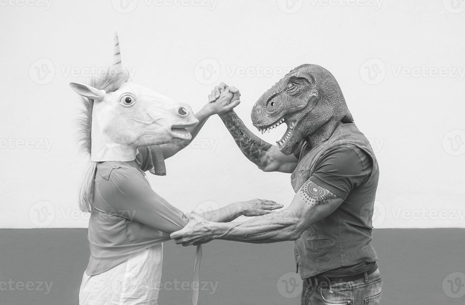 Crazy couple dancing and wearing dinosaur and unicorn mask - Senior trendy people having fun masked at carnival parade - Absurd, eccentric, surreal, fest and funny masquerade concept photo
