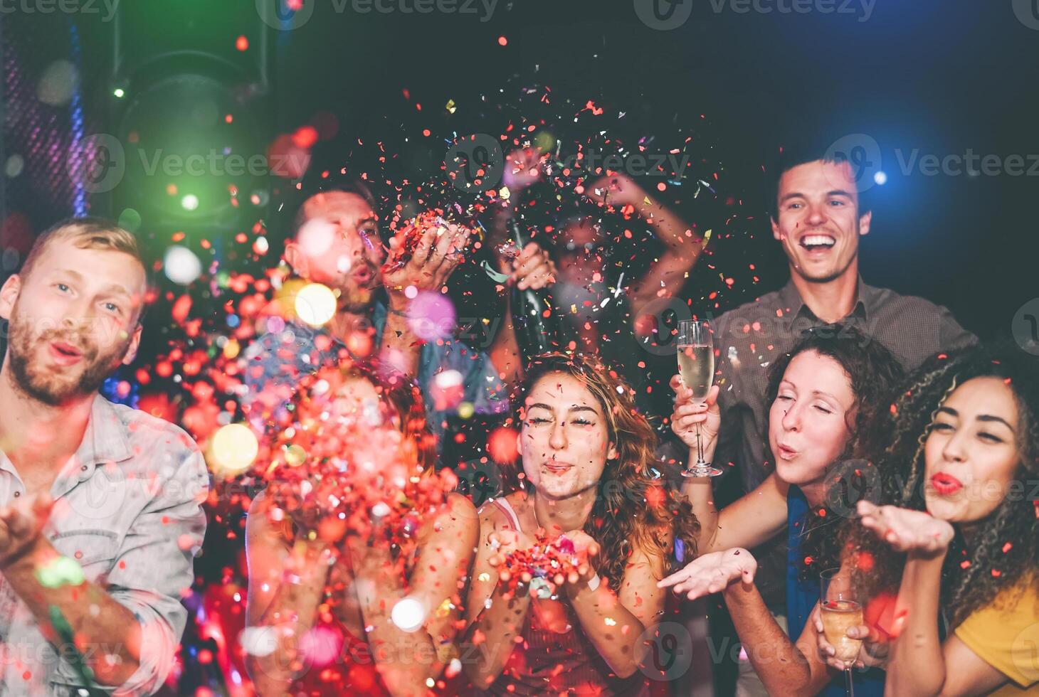 Happy friends doing party throwing confetti in nightclub - Group young people having fun celebrating new year holidays together in disco club - Youth culture entertainment lifestyle concept photo