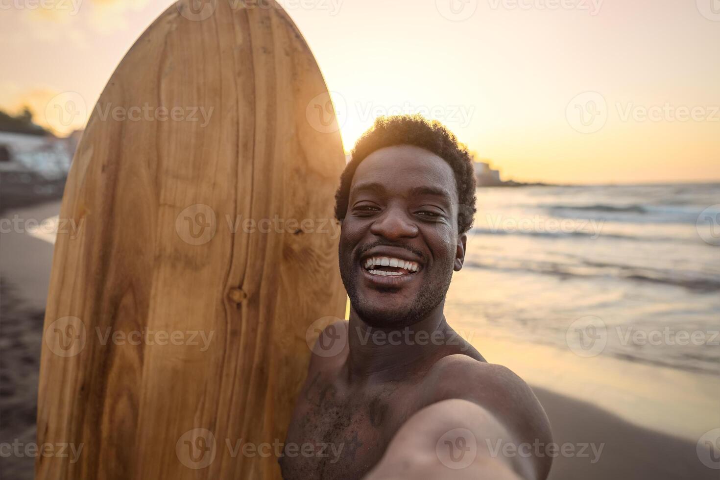 Happy afro surfer having fun taking selfie during sunset time - African man enjoying surf day - Extreme sport lifestyle people concept photo