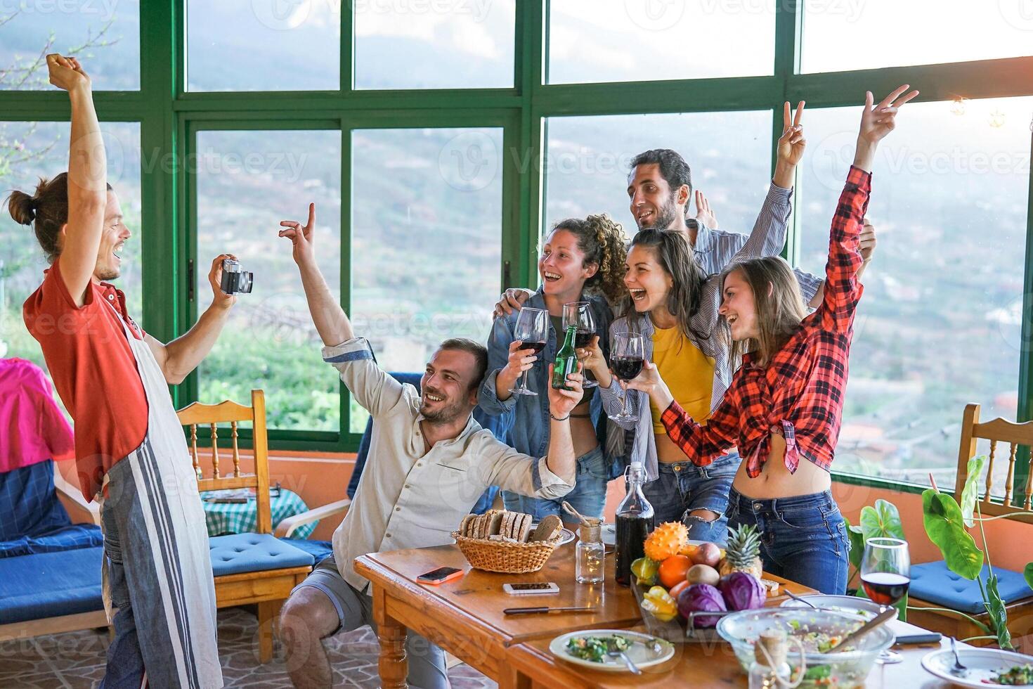 Group of friends taking photo with old vintage camera at dinner eating fresh vegetables and drinking red wine - Happy people dining and having fun together in villa farm house - Friendship concept