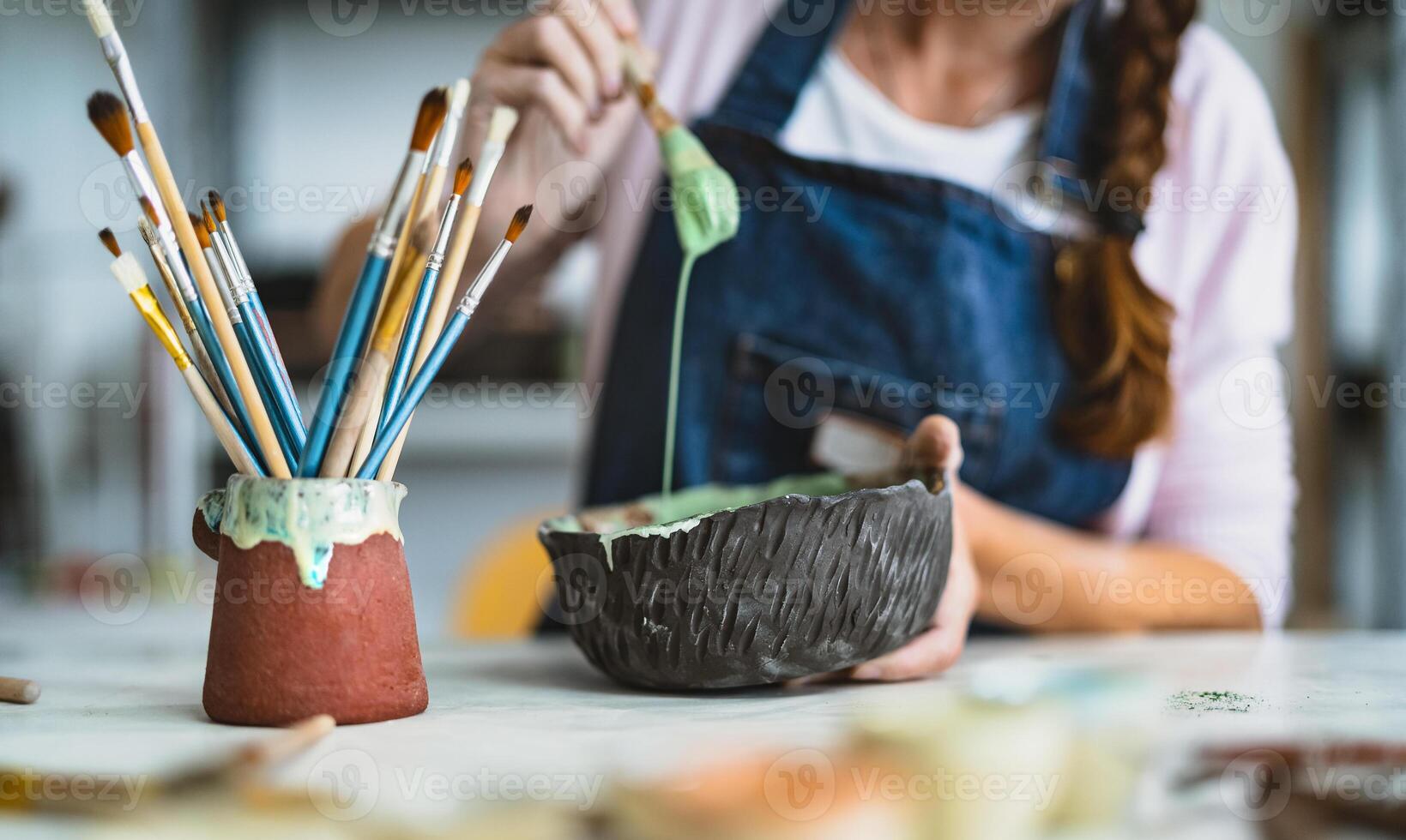 Woman mixing paint with brush inside ceramic bowl in workshop studio - Artisan work and creative craft concept photo