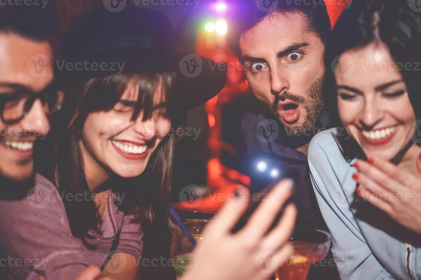 Happy friends having fun watching on mobile smartphone in jazz bar - Group young people using new technology trendy social media apps in club entertainment - Youth millennial and technology concept photo