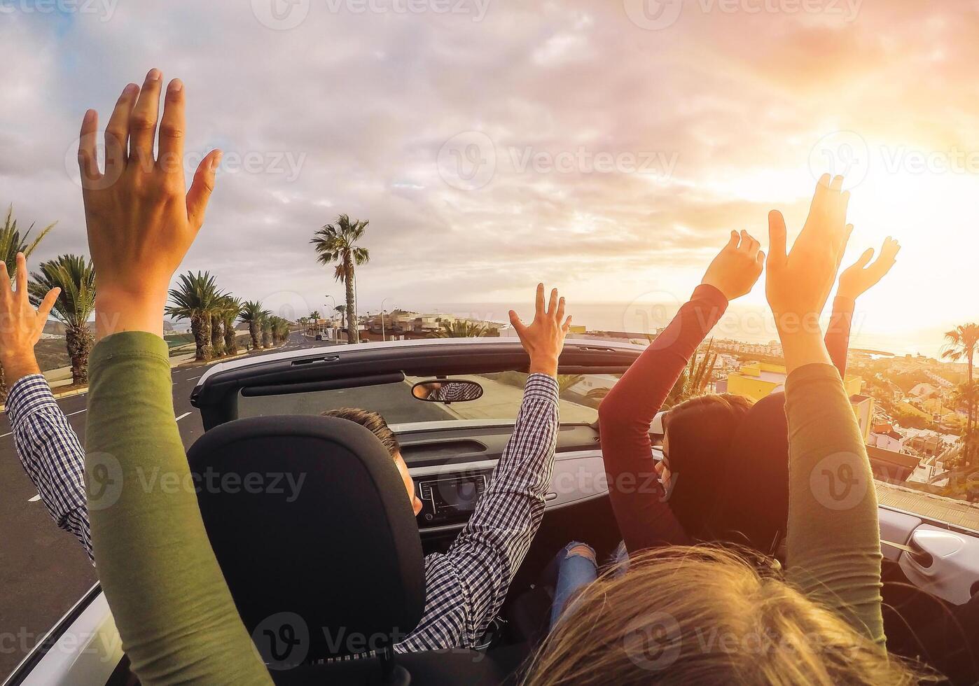 Happy friends having fun in convertible car at sunset in vacation - Young people making party and dancing in a cabrio auto during their road trip - Friendship, travel, youth lifestyle concept photo