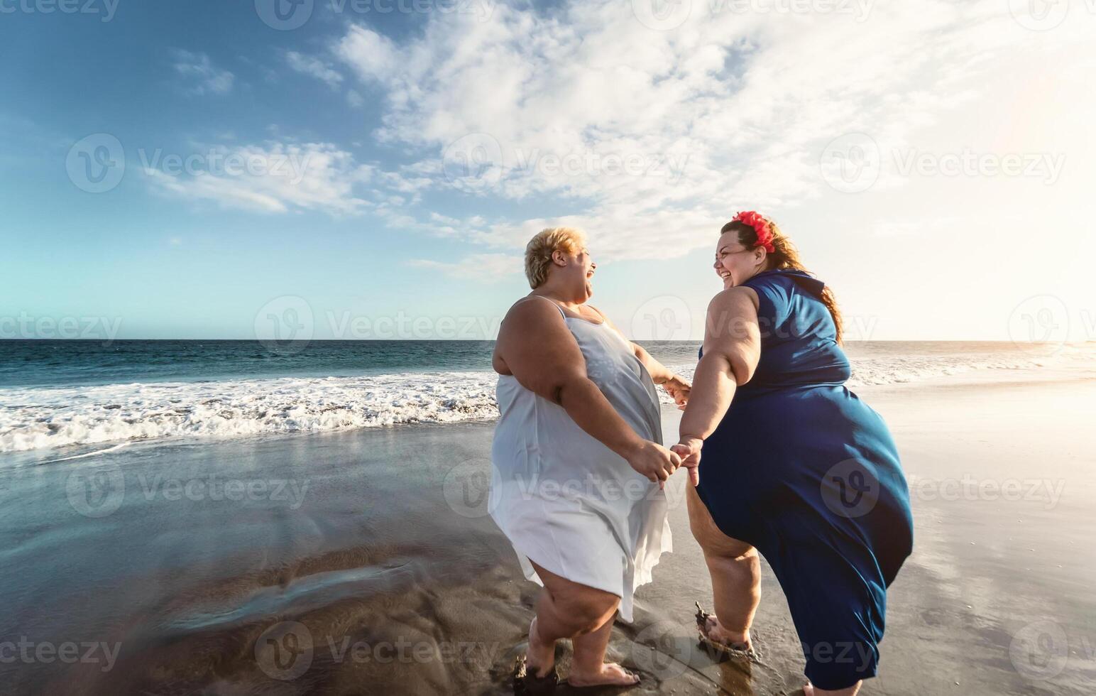 Happy plus size women dancing on the beach - Curvy overweight girls having fun during vacation in tropical destination - Over size confident people lifestyle concept photo