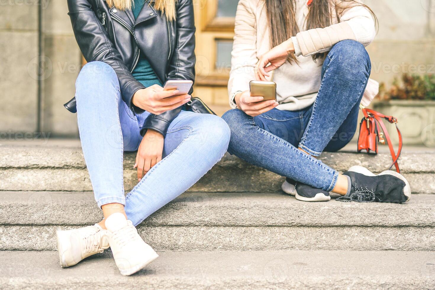 Young women using mobile phone while sitting on stairs of an urban area - Young generation addicted to new smart phones electronic devices - Concept of Social, technology, lifestyle photo