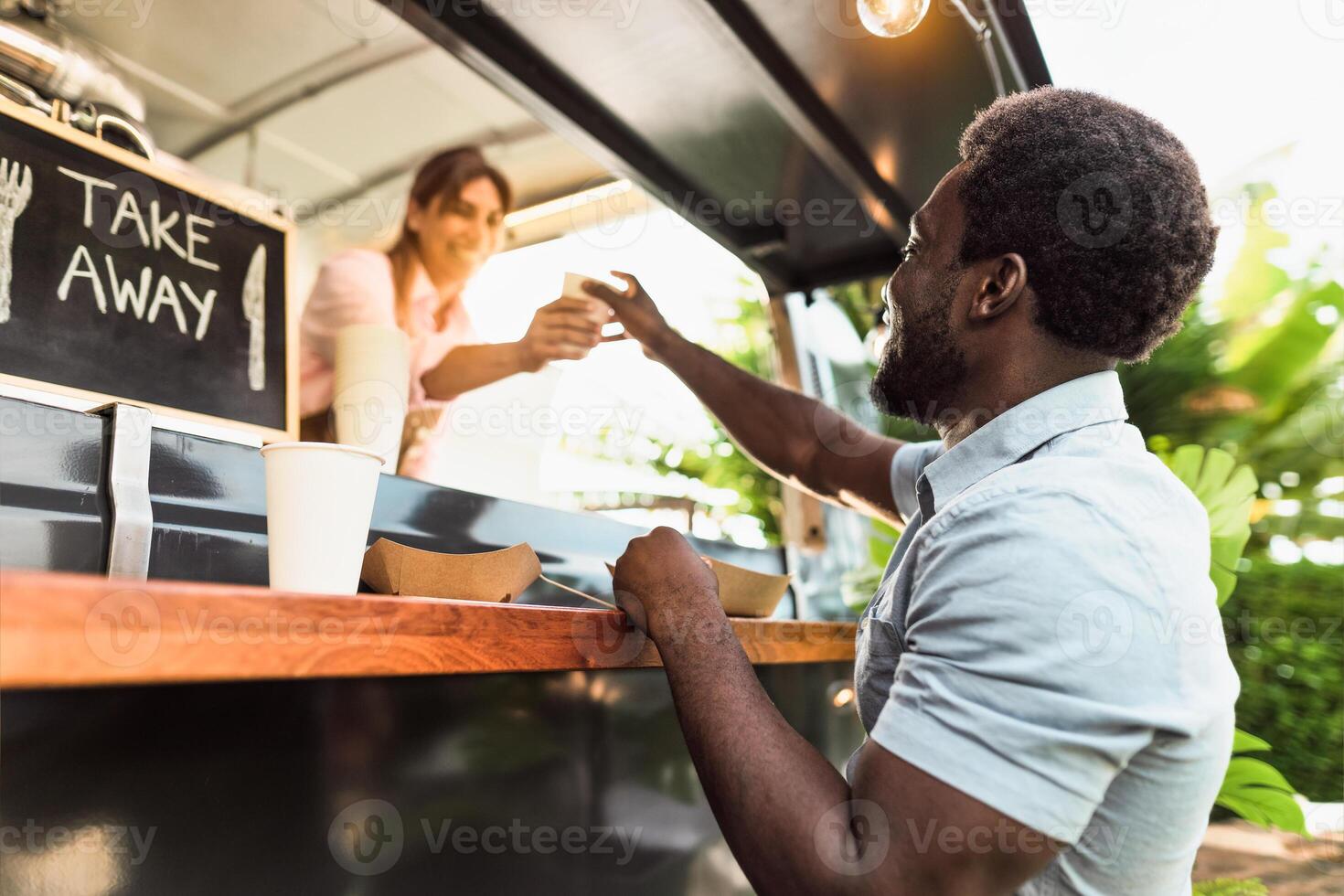 Young African man buying meal from food truck - Modern business and take away concept photo
