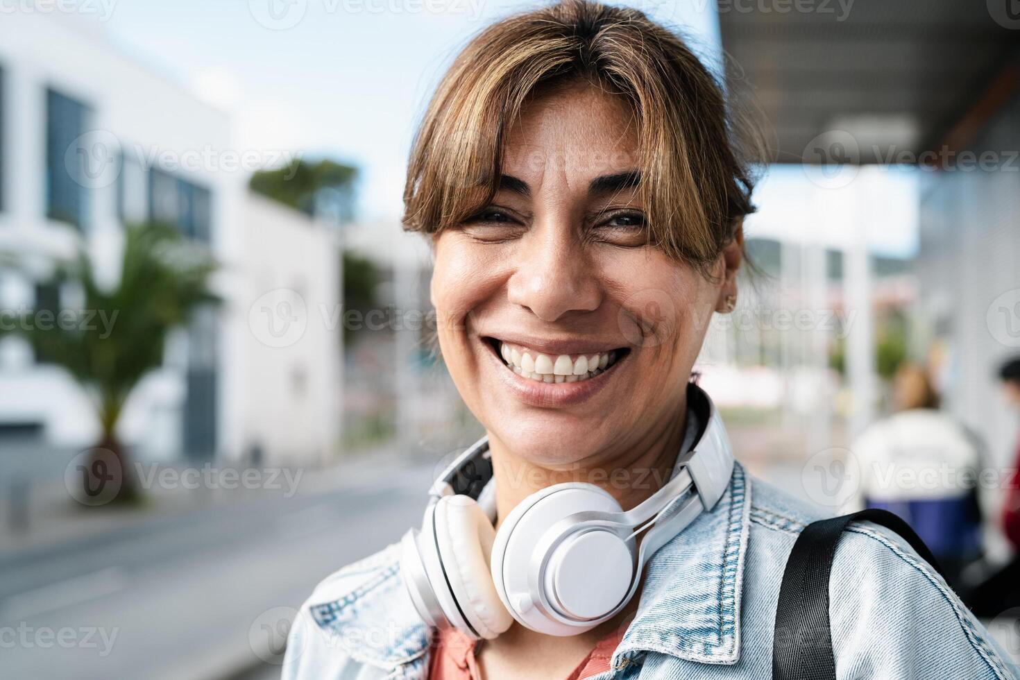 Happy Latin woman smiling in front of camera while waiting at bus station in the city photo