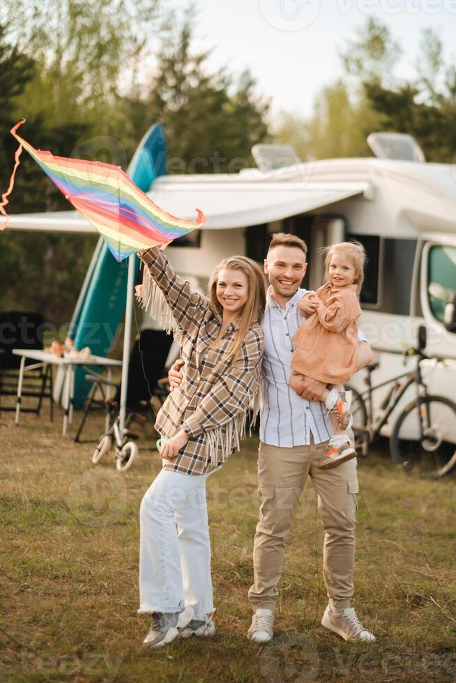 Happy parents with their child play with a kite near their motorhome in the forest photo