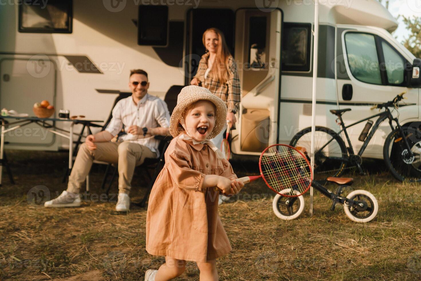a young family is resting next to their mobile home.A girl plays bambinton near a mobile home photo