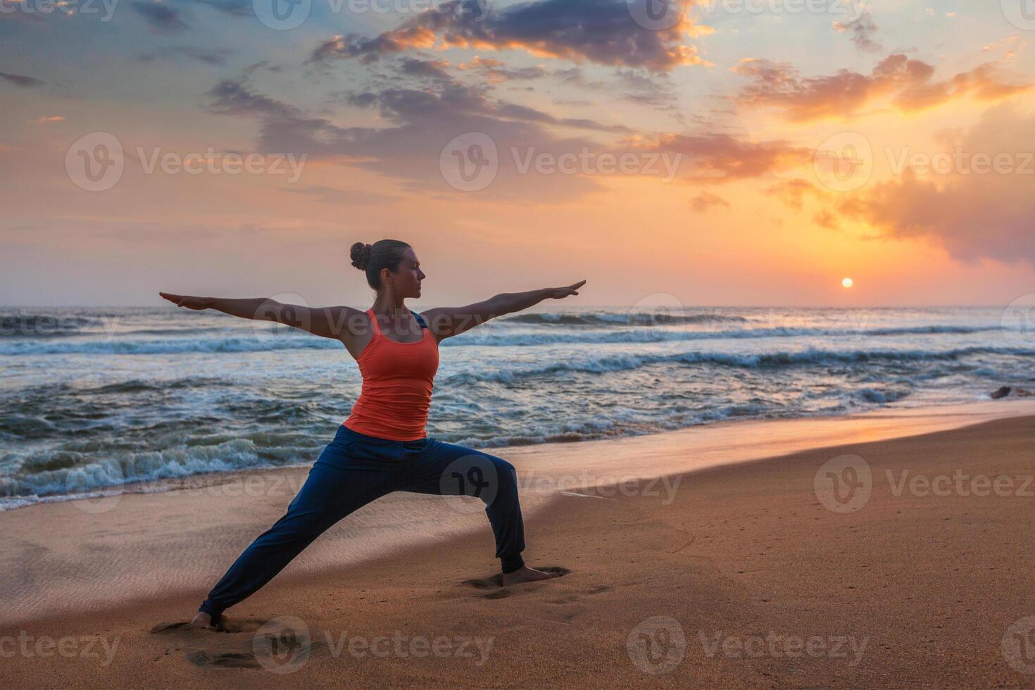 Woman doing yoga asana Virabhadrasana 1 Warrior Pose on beach on photo