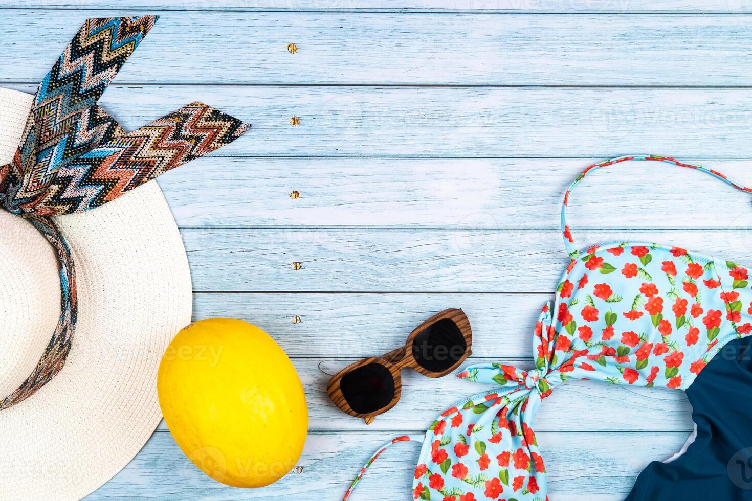 Top view of a straw white hat with glasses and a swimsuit, lying on a blue wooden background.Summer vacation concept photo