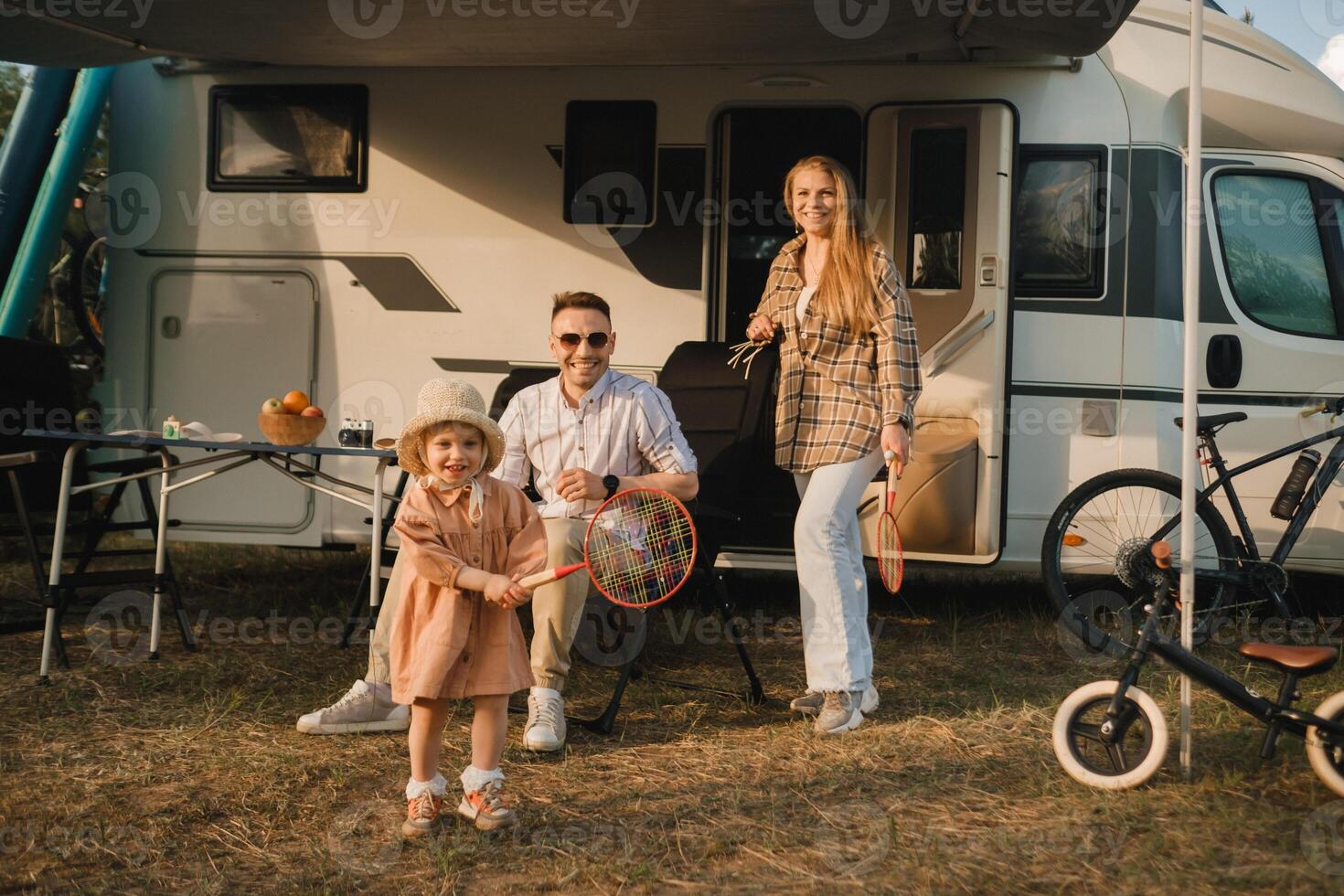 a young family is resting next to their mobile home.A girl plays bambinton near a mobile home photo