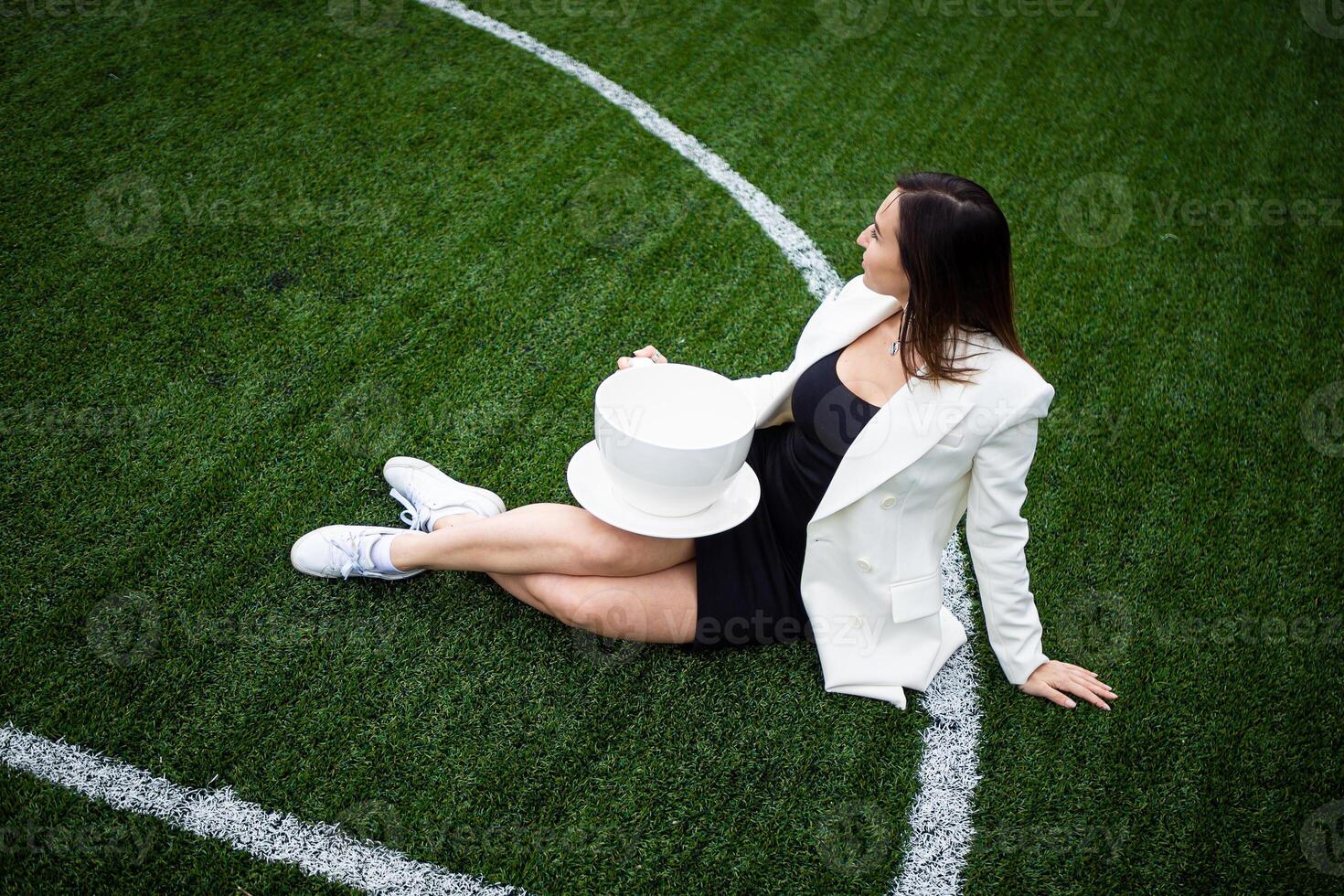 A business woman with a large cup, sitting on a green lawn in the park. photo