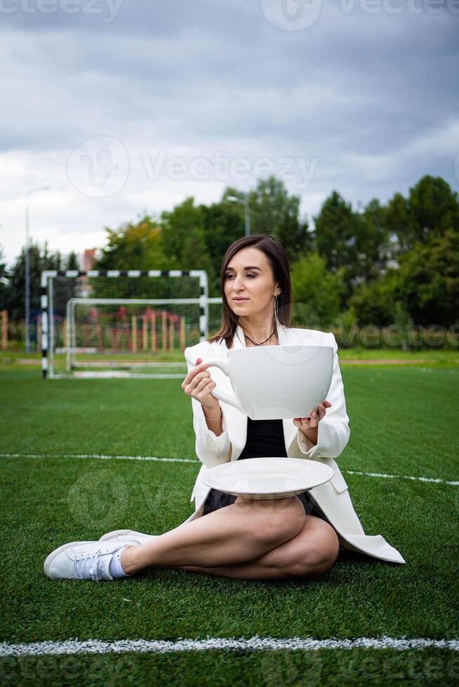 un negocio mujer con un grande taza, sentado en un verde césped en el parque. foto