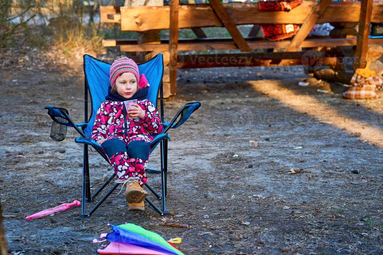 Preschool child in colorful overalls sitting in a folding chair on a picnic photo