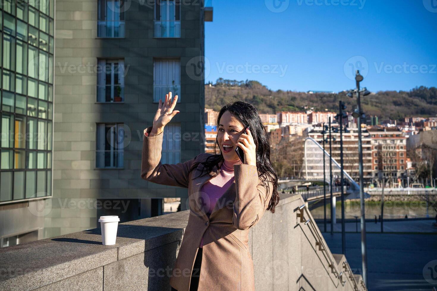 Smiling young woman waves while having a conversation with her mobile phone photo