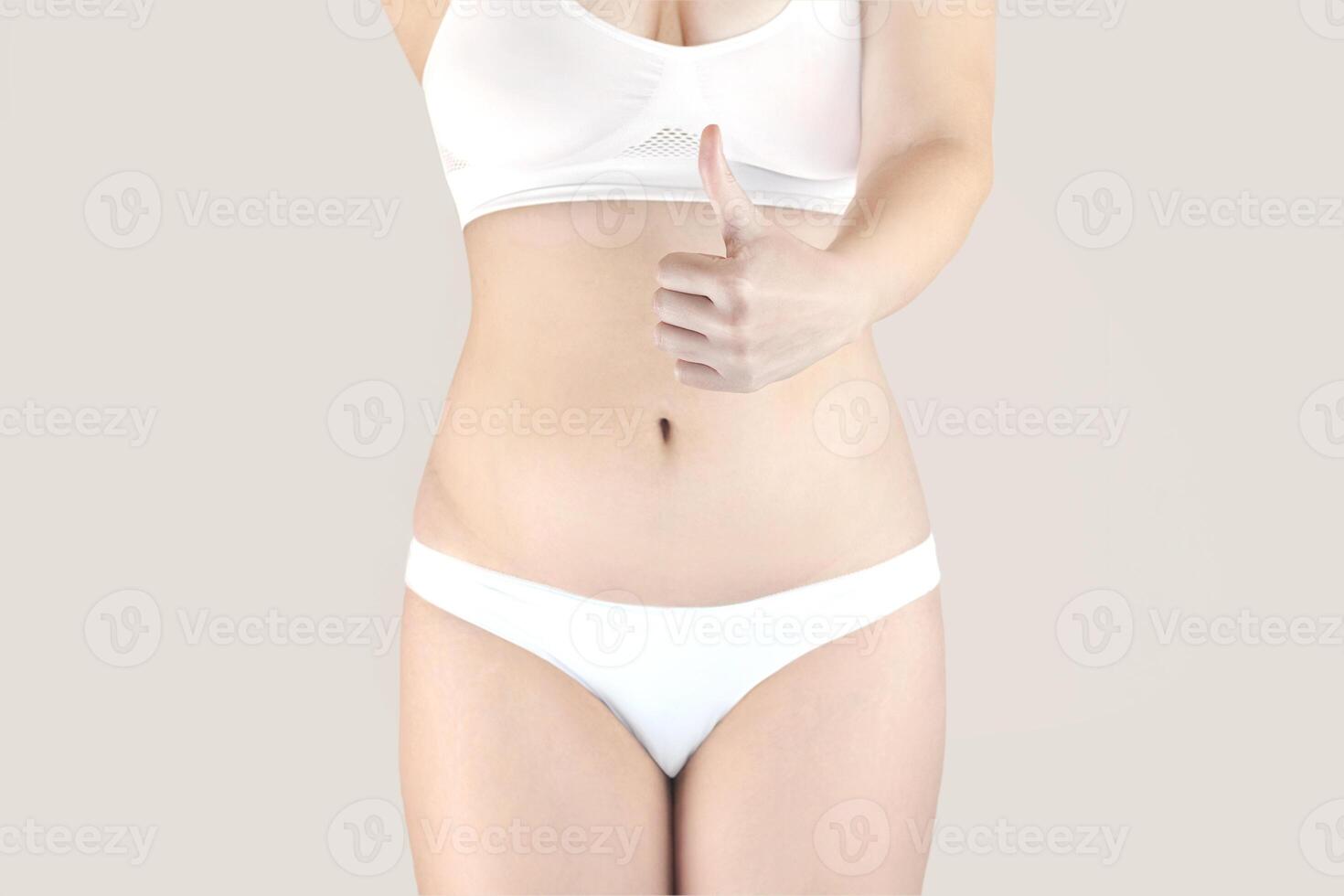 A slender woman likes her figure and is happy with her body. She stands in white underwear and shows a thumbs up. A woman is happy that she has lost weight photo