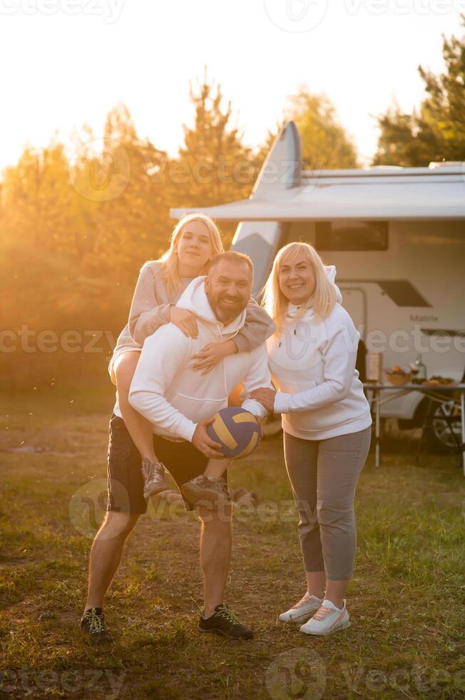 Happy parents with their child playing with a ball near their mobile home in the woods photo