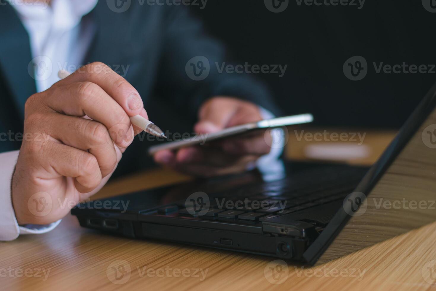 Close-up of a businessman working with a notebook computer and using a pen to take notes and using a mobile phone, smartphone, chatting, working in the office. photo