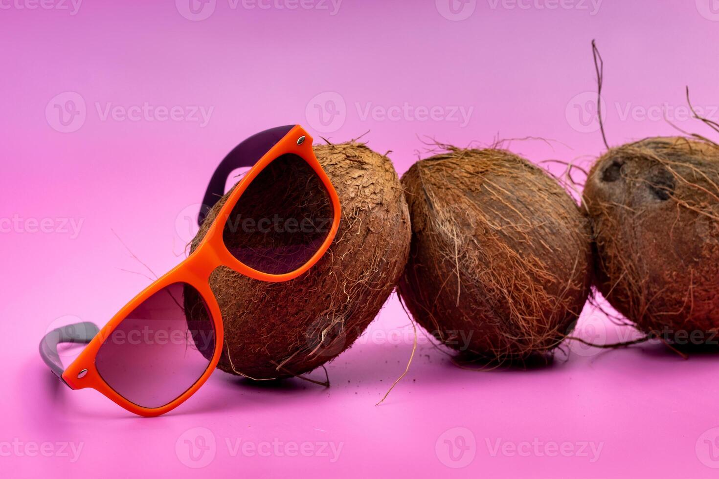 three whole coconuts and orange glasses on a pink background photo