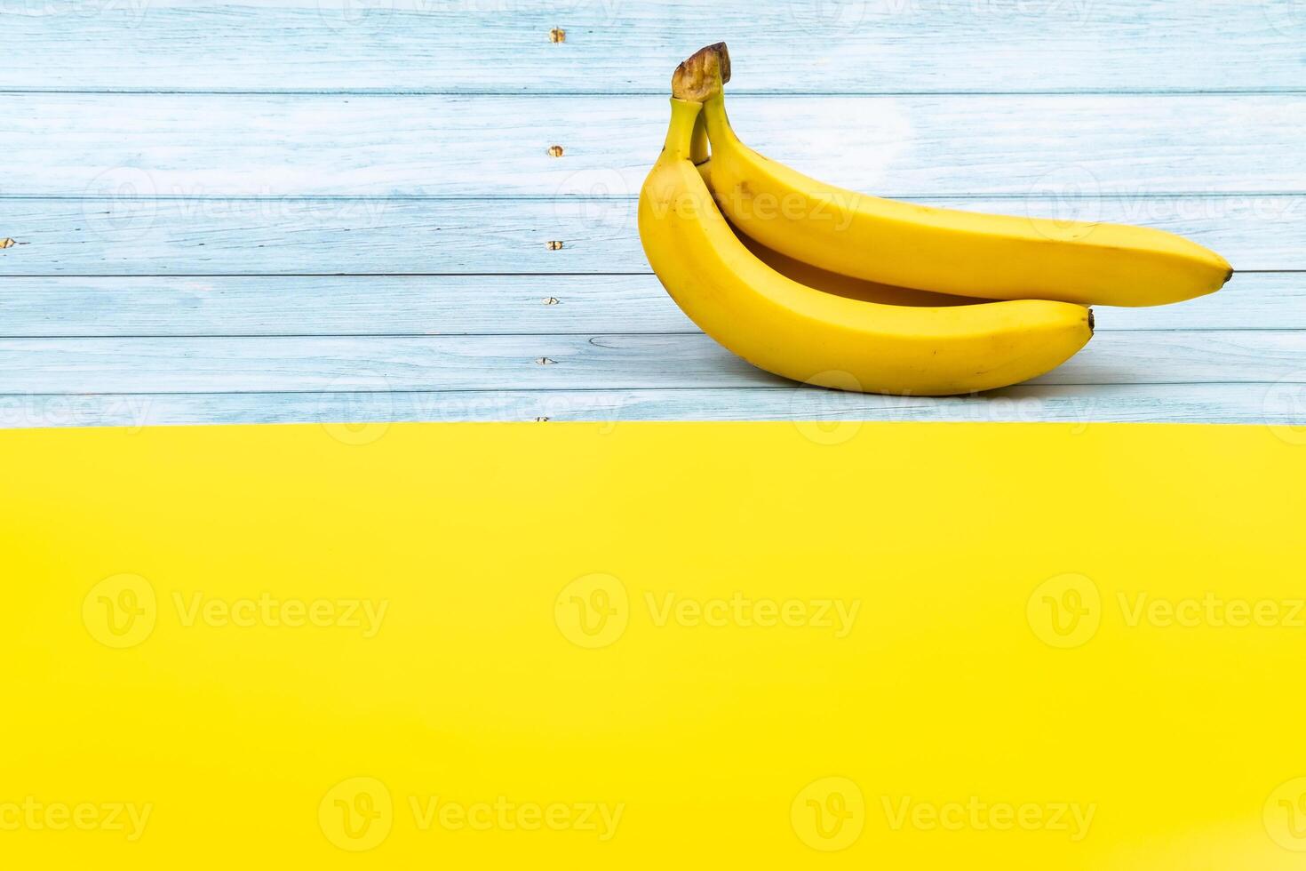 Yellow bananas lie on a blue wooden background and a yellow background photo