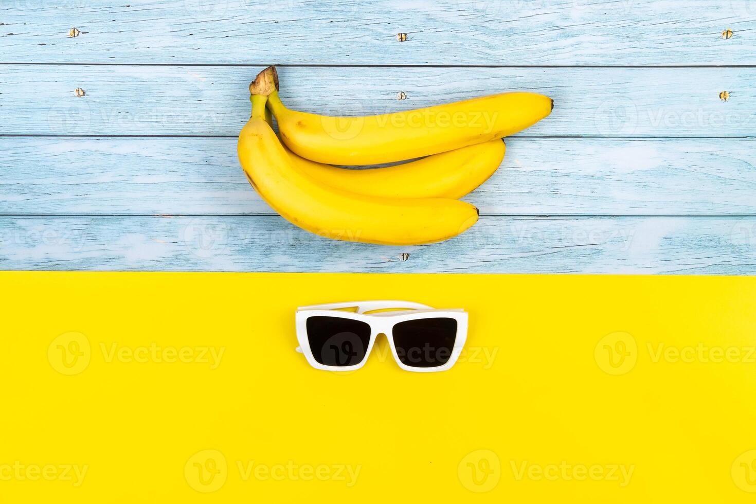 Yellow bananas and sunglasses lie on a blue wooden background and a yellow background photo