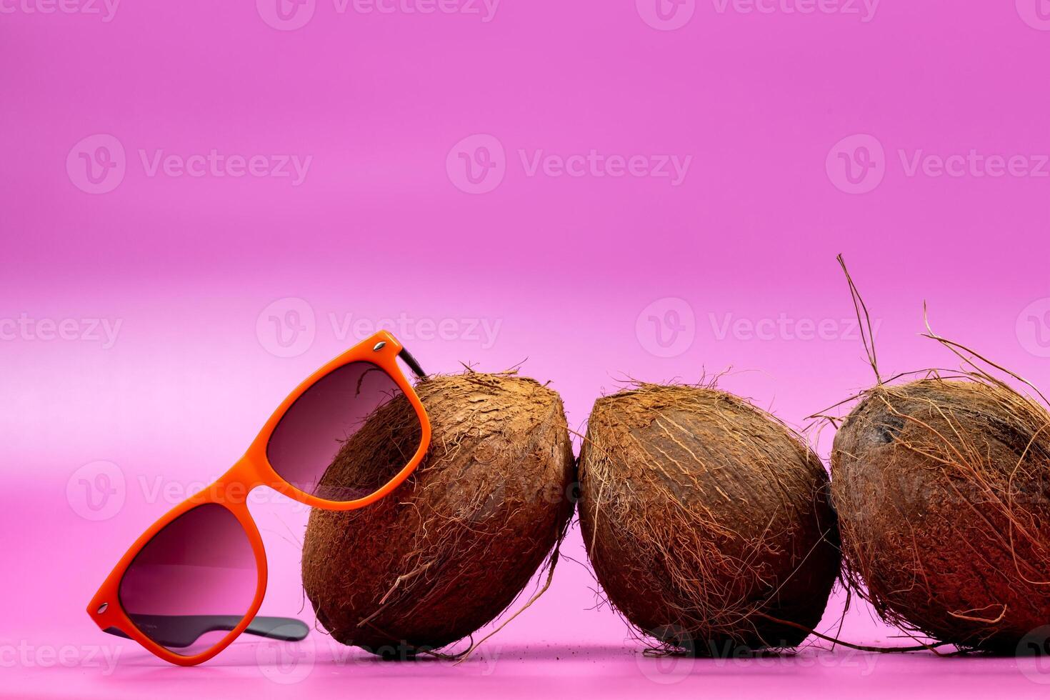 three whole coconuts and orange glasses on a pink background photo