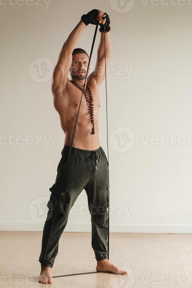 A man with a naked torso is engaged in strength fitness using a rubber loop indoors photo