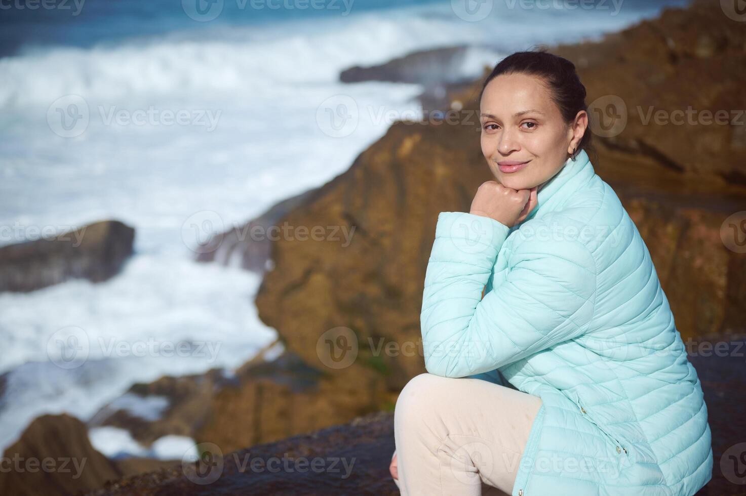 contento mujer sonriente a cámara, sentado en el acantilado y disfrutando hermosa ver de atlántico océano. gente. excursión turismo. foto