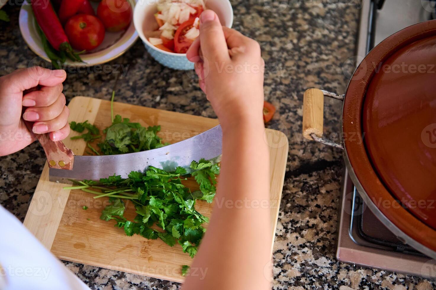 Close-up detail of woman chef hands holding a large knife and chopping fresh green parsley on a wood chopping board photo