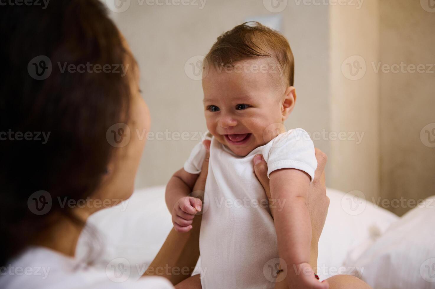 Adorable smiling newborn baby boy in tender embrace of his loving caring mother. Babyhood and infancy concept photo