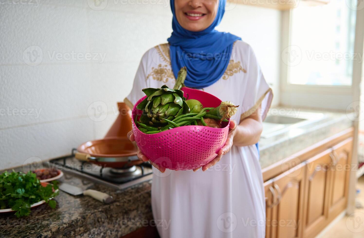 Details on a pink bowl with washed fresh organic vegetables in the hands of a housewife in hijab and authentic dress photo