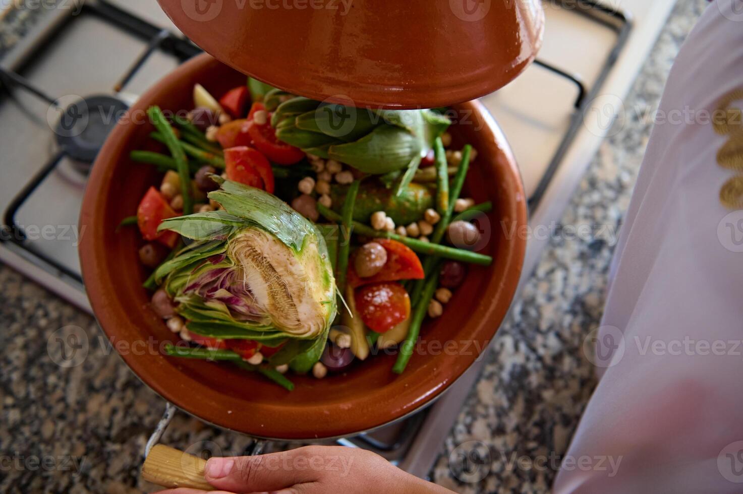 Directly above fresh potatoes, green beans and artichoke steaming in traditional clay pot -Tagine, steaming on a stove photo