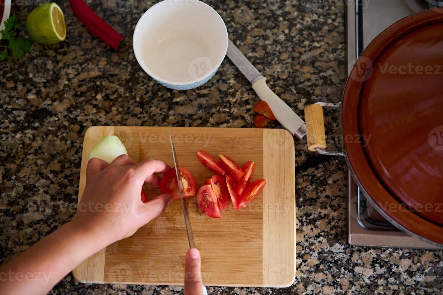 Close-up view from above of a cook chef, using kitchen knife slicing chopping cutting tomatoes on a wooden board photo