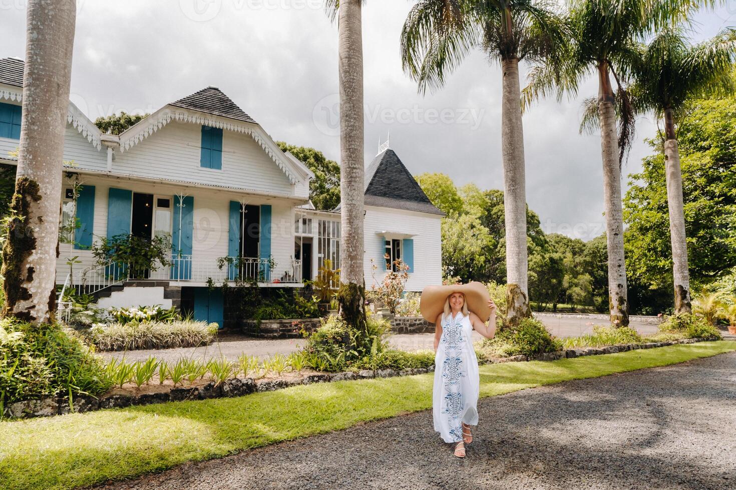 el mujer en el grande sombrero es sonriente. un hermosa niña en un grande sombrero y blanco vestir sonrisas fuera de un antiguo colonial edificio en el isla de Mauricio foto