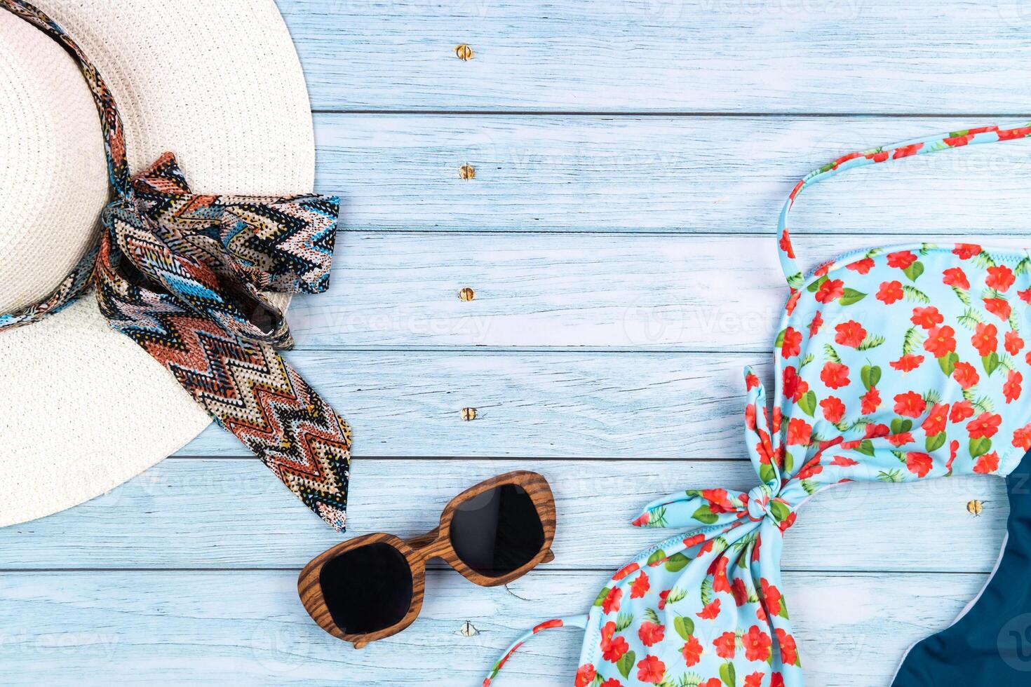 Top view of a straw white hat with glasses and a swimsuit, lying on a blue wooden background.Summer vacation concept photo