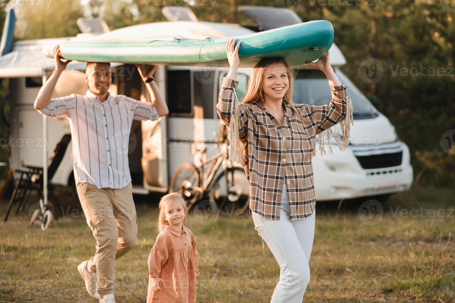 a young family is playing next to their mobile home. Dad and mom are carrying a sup board and daughter is walking next to photo