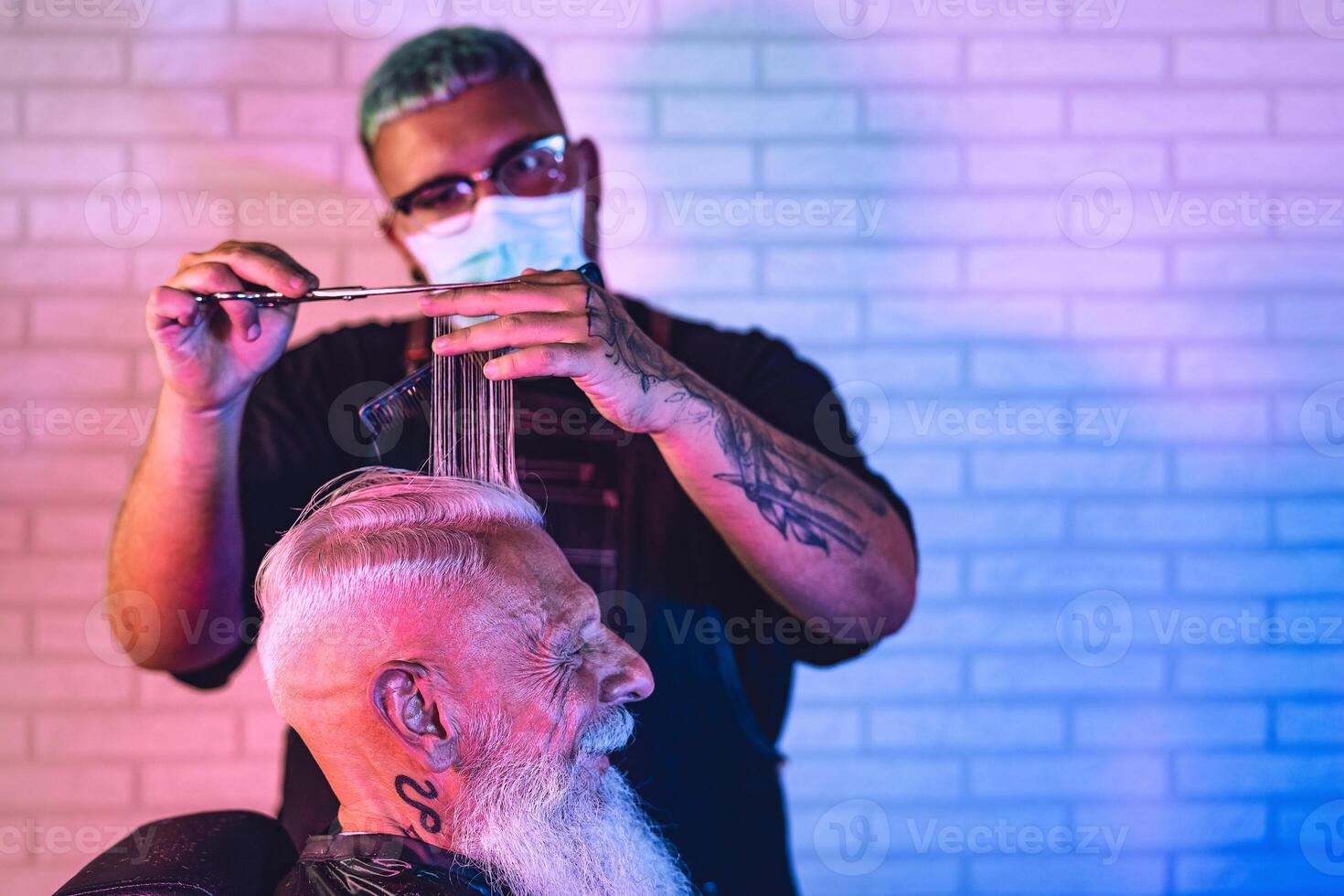 Male hairdresser cutting hair to hipster senior client while wearing face surgical mask - Young hairstylist working in barbershop during corona virus outbreak - Health care and haircut salon concept photo