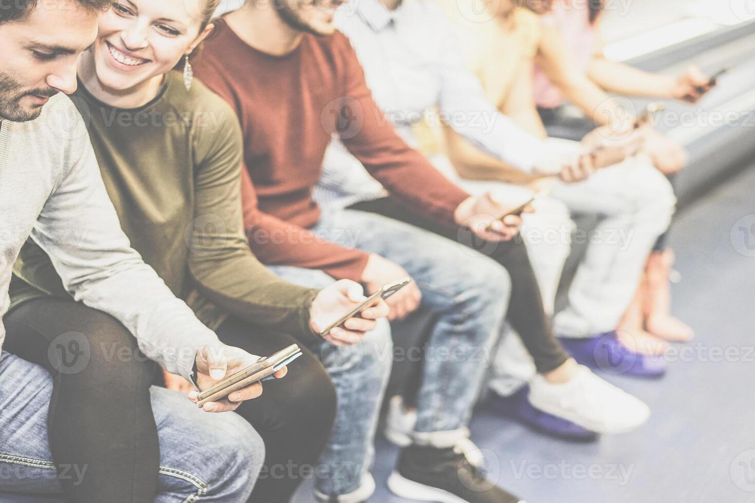Group of friends using together their mobile smart phones while sitting in underground - Young people surfing on social network on phone - Concept of youth addiction to new technology photo