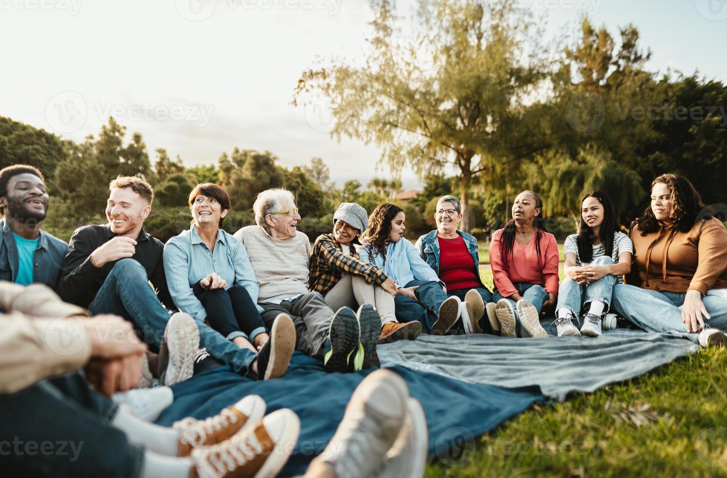 Happy multi generational people having fun sitting on grass in a public park - Diversity and friendship concept photo