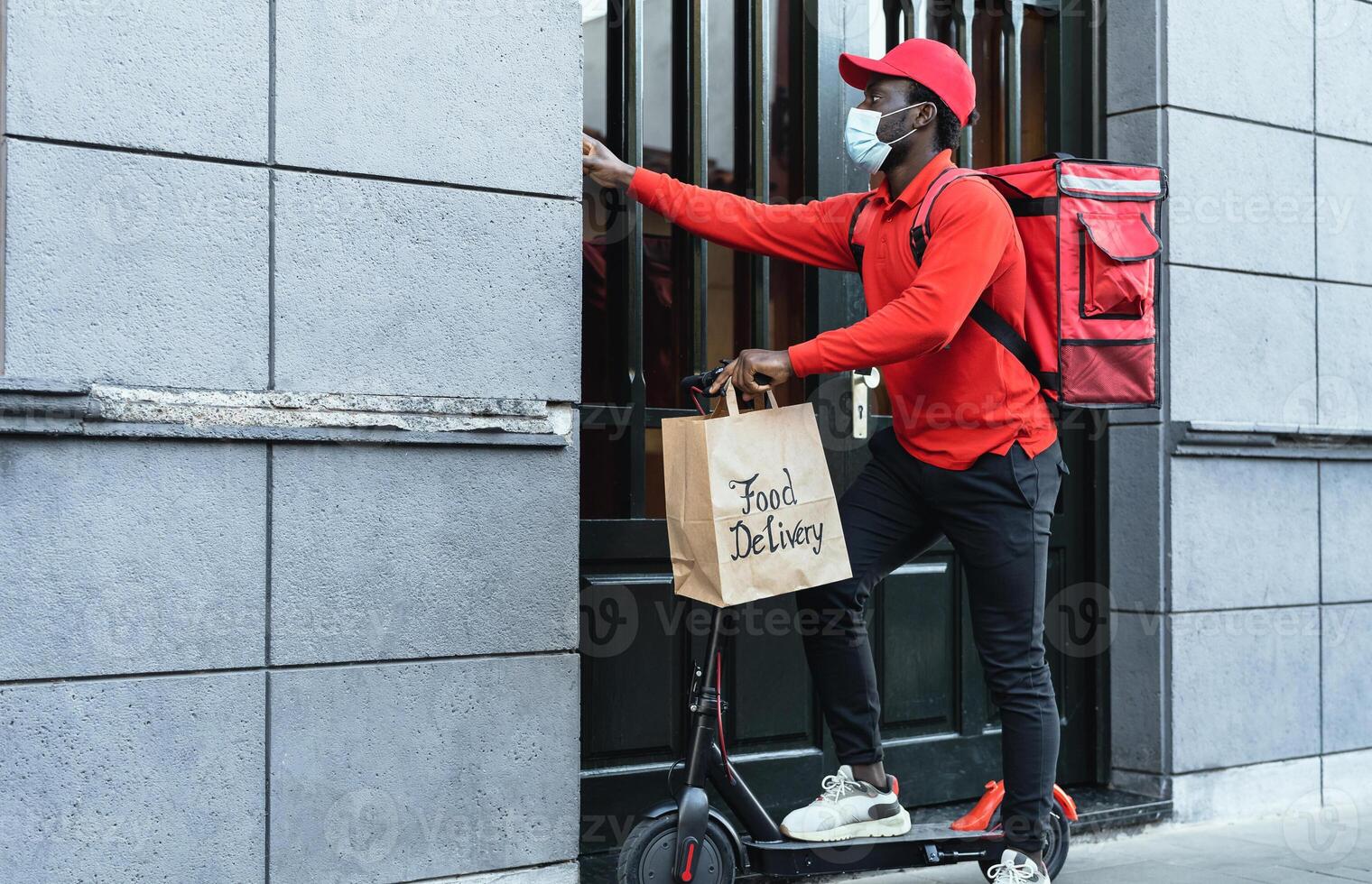 African rider man delivering meal to customers with electric scooter while wearing face mask during corona virus outbreak - Ecological fast delivery food concept photo