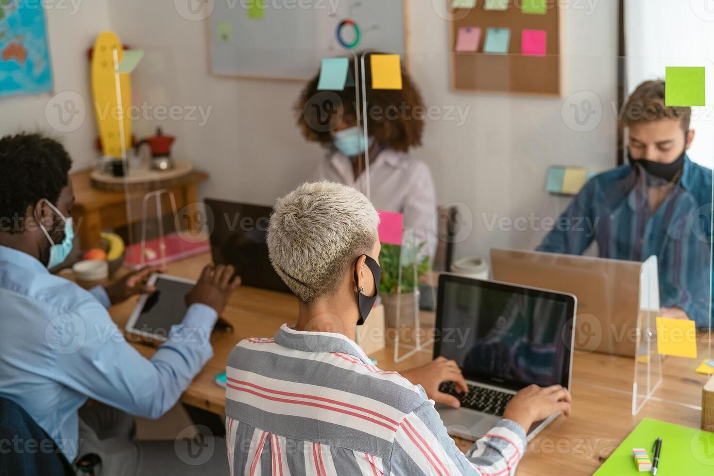 Young multiracial people using computer in co-working creative space while wearing face mask - Health and business technology concept photo