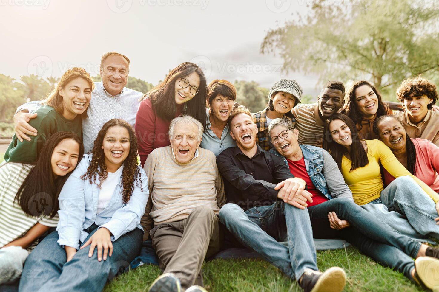 Happy multigenerational people having fun sitting on grass in a public park photo