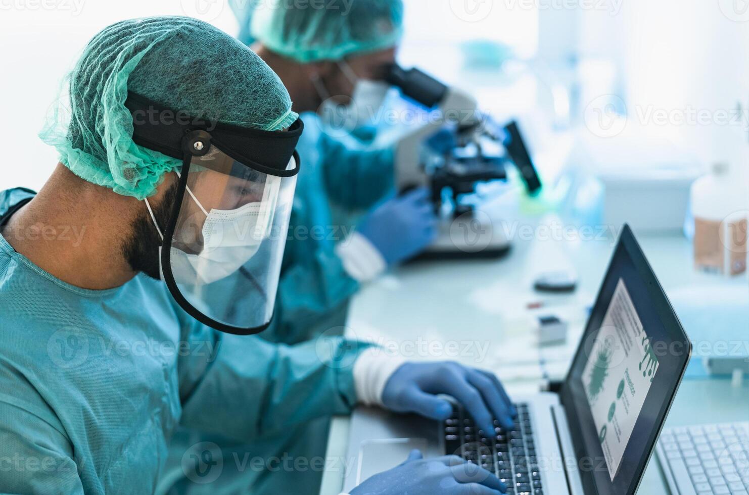Doctors wearing personal protective equipment working in laboratory using computer and examining coronavirus through microscope - Science and technology concept photo