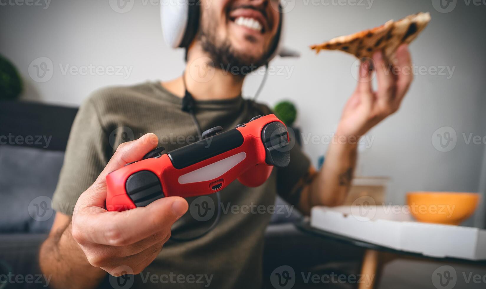 Happy man playing online video games while eating pizza fast food - Young gamer having fun on new technology console - Gaming entertainment and youth millennial generation lifestyle concept photo