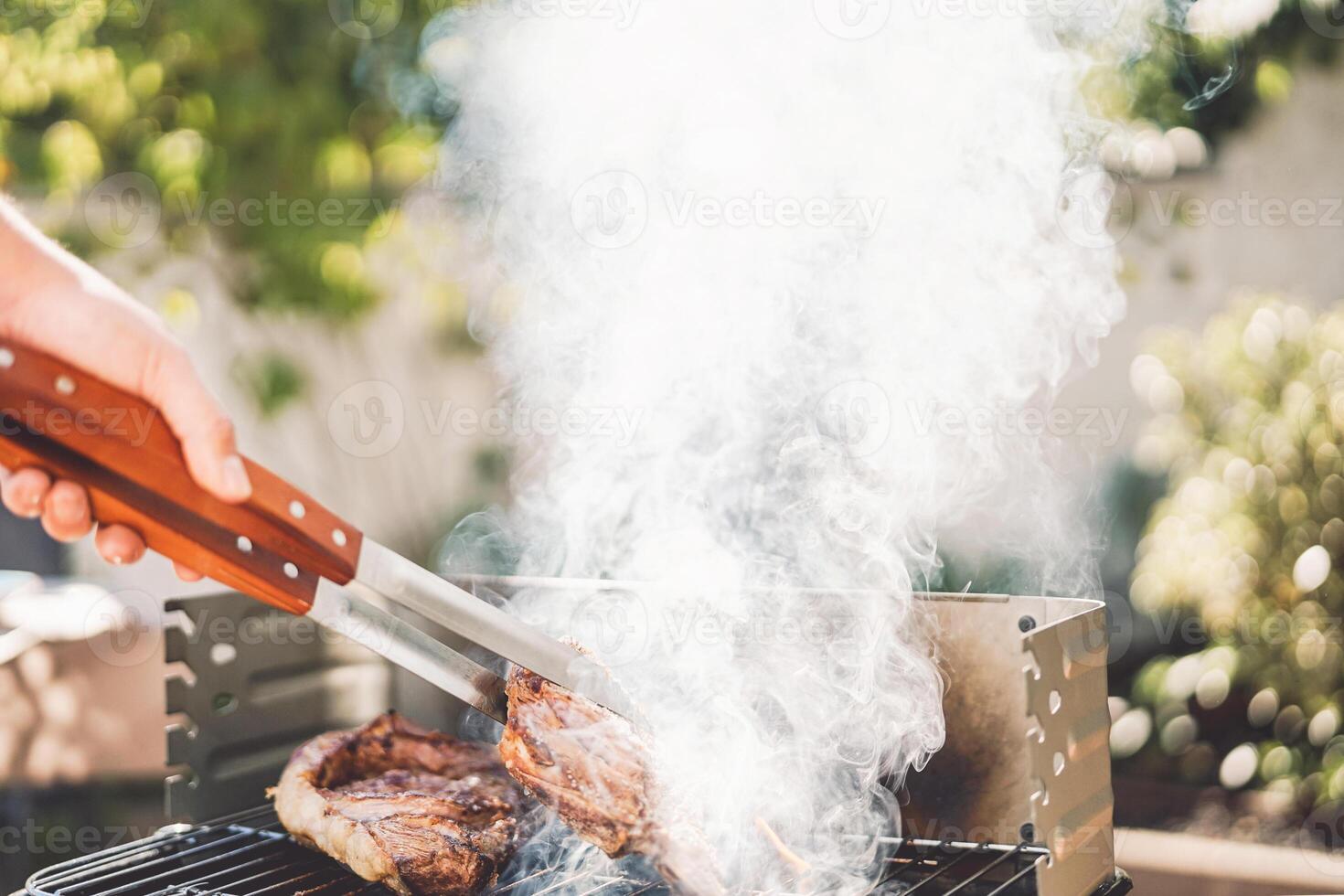 Man chef grilling beef steak at barbecue dinner party outdoor - Close up male hand cooking meat on bbq for family in the garden - Food, weekend activities and people lifestyle concept photo