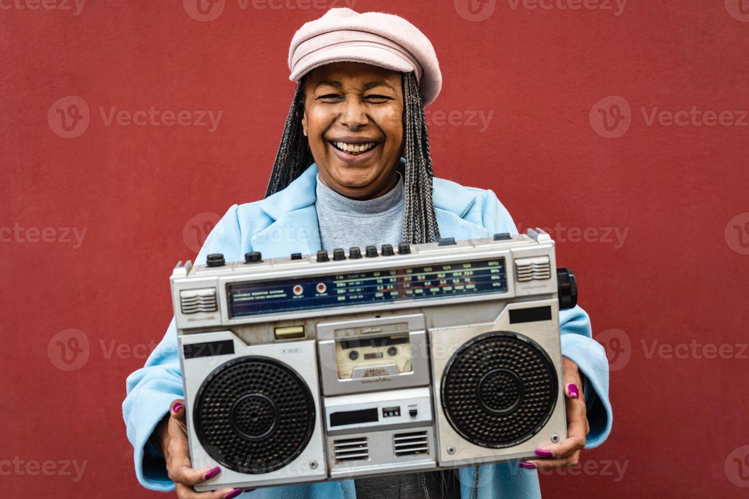 Happy trendy senior African woman having fun listening to music with vintage boombox stereo photo