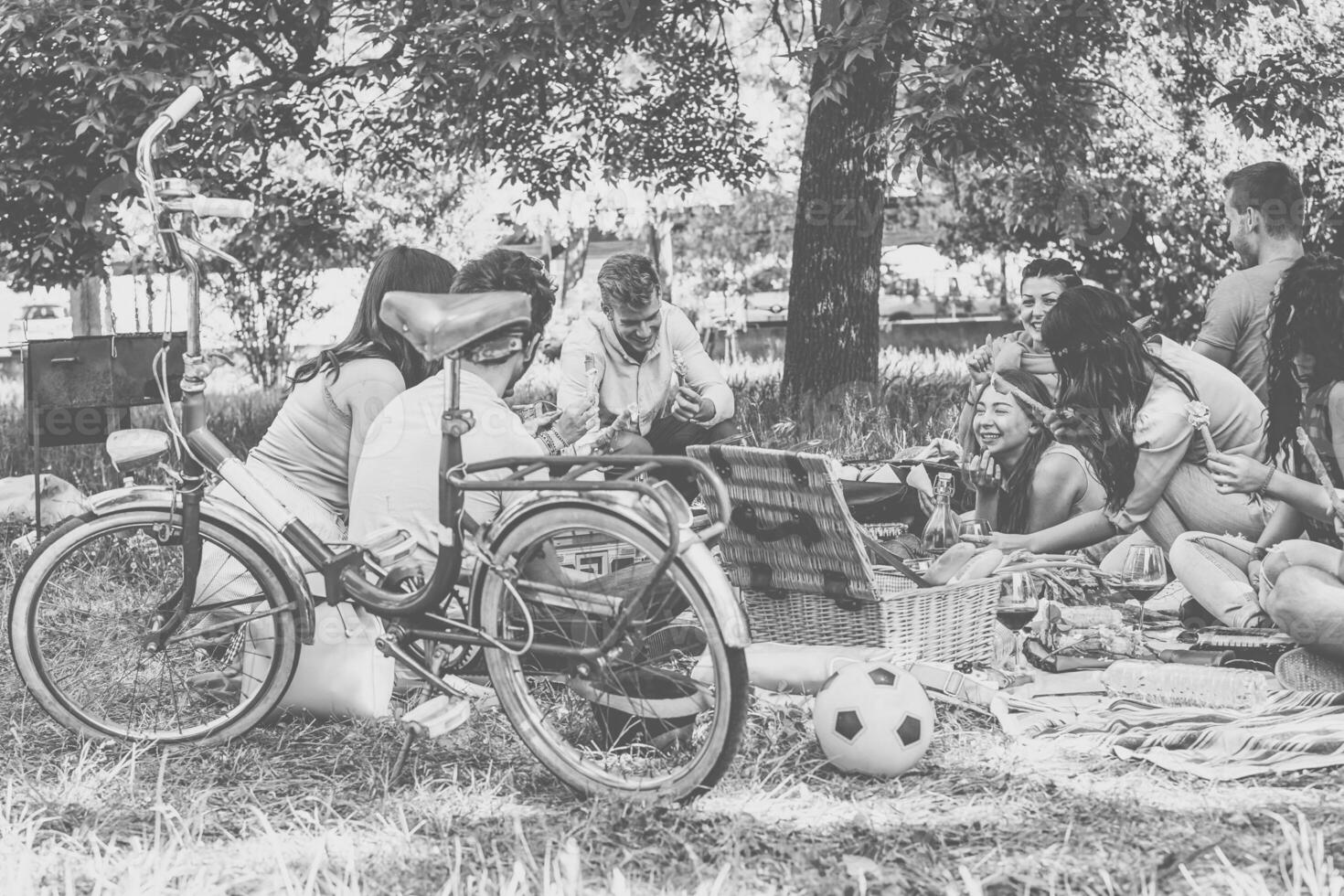 Group of friends enjoying a picnic while eating and drinking red wine in countryside - Happy people having fun together - Concept of friendship, lifestyle, food and drinks - Black and white editing photo